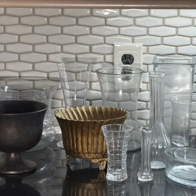 Assortment of vintage glassware and decorative vessels, including a footed brass planter, a dark metal chalice, and various clear glass...