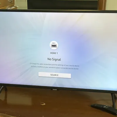 Samsung flat-screen television with remote, shown powered on and resting on a wooden surface.