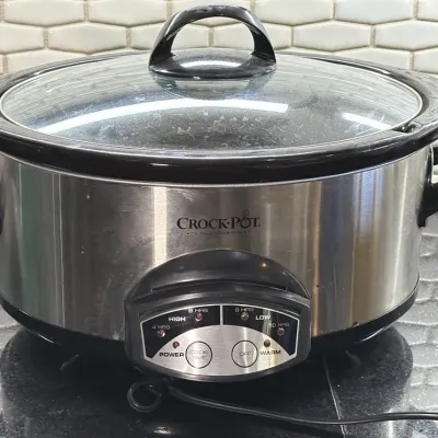 Crock-Pot stainless steel slow cooker with a glass lid, black handles, and digital control panel.