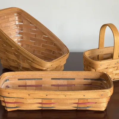 Three vintage Longaberger woven wood baskets, including a small handled basket, a sloped organizer basket, and a long rectangular basket...