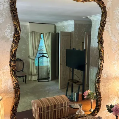 Large vintage wall mirror featuring an ornate, wavy gilt frame with scrollwork details, mounted above a dresser.