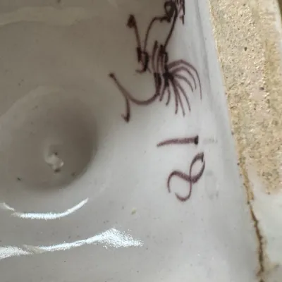 Close-up of a hand-painted maker's mark and the number 18 on the glazed underside of a ceramic piece.