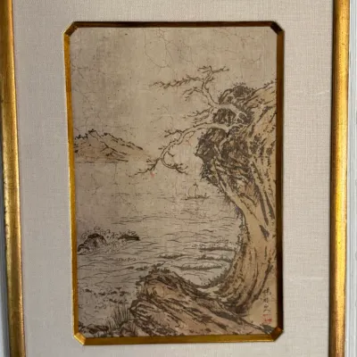 Framed East Asian ink wash landscape painting on paper, depicting a coastal scene with a gnarled tree, rocky cliffs, and a distant...