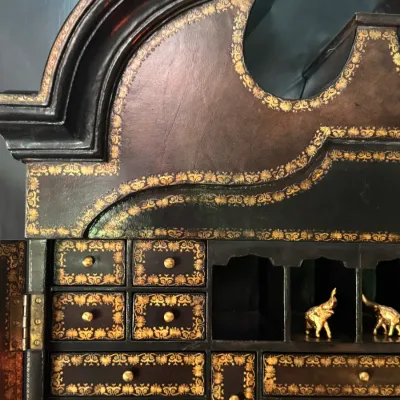 Detail of a vintage secretary desk featuring ornate gold-leaf stenciled borders, multiple small drawers with brass pulls, and open cubbies.