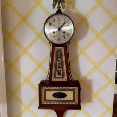 Vintage Seth Thomas banjo wall clock featuring a mahogany case, brass eagle finial, and decorative painted glass panels.