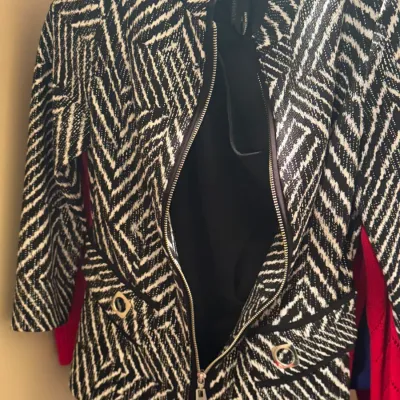 Frank Lyman black and white geometric patterned zip-up jacket with grommet details on the faux pockets, shown hanging in a closet.