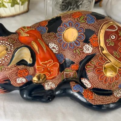 Vintage Japanese Kutani porcelain sleeping cat figurine, featuring intricate hand-painted floral and geometric patterns in red, gold, and...