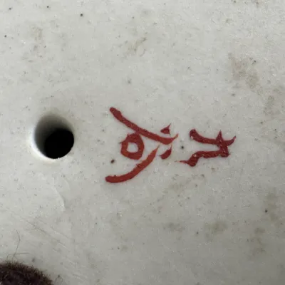 Close-up of a red painted artist signature or maker's mark on the unglazed ceramic base of an art piece.