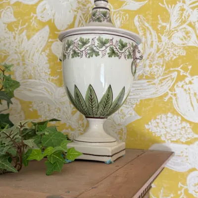 Vintage Italian ceramic lidded urn featuring hand-painted green leaves, grapevines, and lion head handles on a square pedestal base.