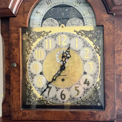 Sligh grandfather clock face featuring an ornate brass and silver-toned dial with a moon phase indicator, housed in a burl wood case.