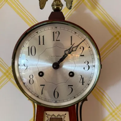 Vintage Seth Thomas banjo clock featuring a silver-tone dial with black Arabic numerals, key-wind holes, and a brass eagle finial.