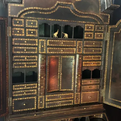 Antique secretary desk cabinet featuring an intricate gold-gilt leather facade with numerous small drawers, cubbies, and faux-book spine...