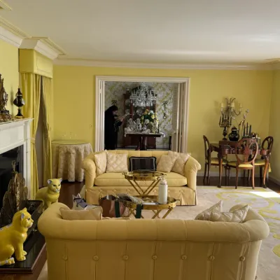 Elegant living room featuring a pair of tufted yellow sofas, a brass tiered coffee table, and a fireplace flanked by yellow ceramic...