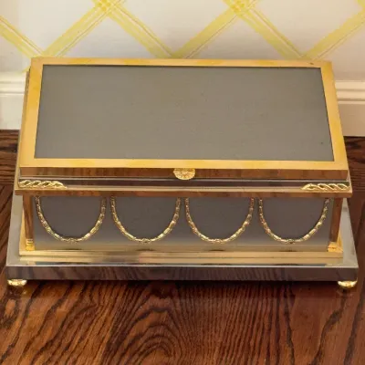 Vintage neoclassical-style jewelry or keepsake box featuring a grey body with gold-tone swags, trim, and ball feet.