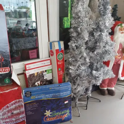Assorted Christmas decorations, including a silver tinsel tree, boxed light-up holiday signs, and a standing Santa Claus figure.