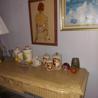 Neoclassical style console table with a fluted apron, displaying vintage ceramic canisters, small decorative figurines, and framed...