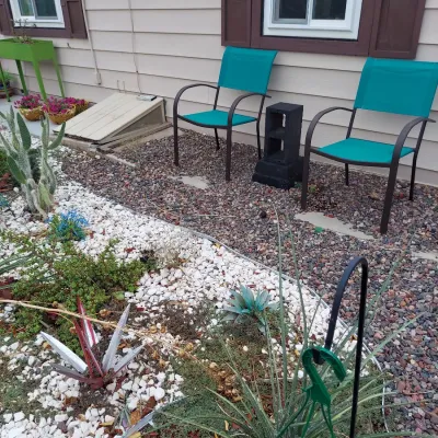 Pair of modern outdoor patio chairs with dark metal frames and vibrant turquoise mesh seating, positioned in a landscaped gravel yard.