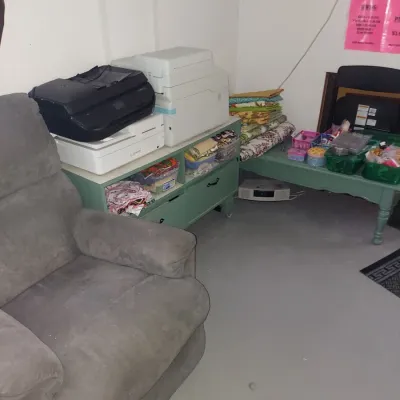 Plush grey microfiber recliner alongside a green painted storage cabinet holding printers and sewing supplies.