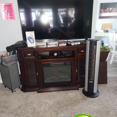 Large flat-screen television sitting atop a dark wood media console with an integrated electric fireplace, flanked by a tall silver tower...