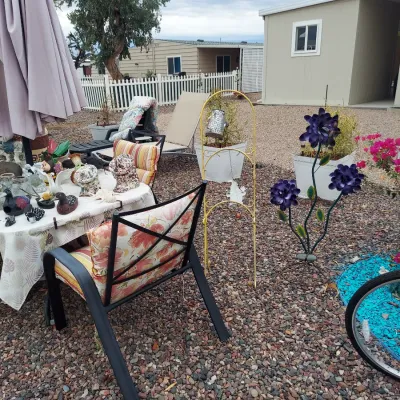 Outdoor patio furniture and garden decor, including a metal armchair with floral cushions, a table with various decorative items, a...
