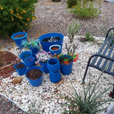 Collection of vibrant blue plastic and ceramic garden planters in various sizes, some containing soil or artificial plants, arranged on...