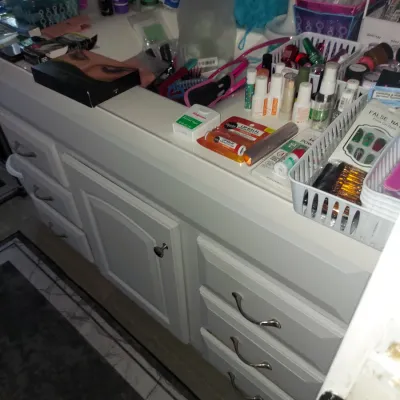 White bathroom vanity cabinet with drawers and a center cupboard, topped with an assortment of cosmetics, toiletries, and personal care...