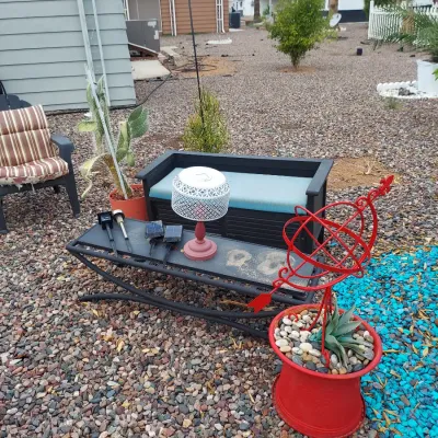 Assorted outdoor patio furniture and decor, including a black metal coffee table, a storage bench with a blue cushion, a red armillary...
