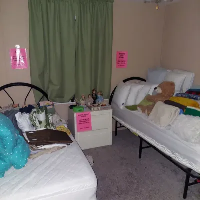 Bedroom featuring two twin beds with metal frames, a white two-drawer nightstand, and various linens, pillows, and decorative items for...