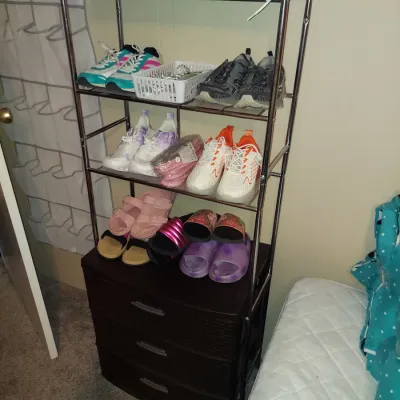 Four-tier chrome wire shoe rack with a dark brown three-drawer plastic storage chest at the base, holding various athletic sneakers and...