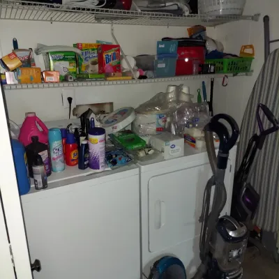 Assorted household items including a white washer and dryer set, upright vacuums, cleaning supplies, and wire shelving.