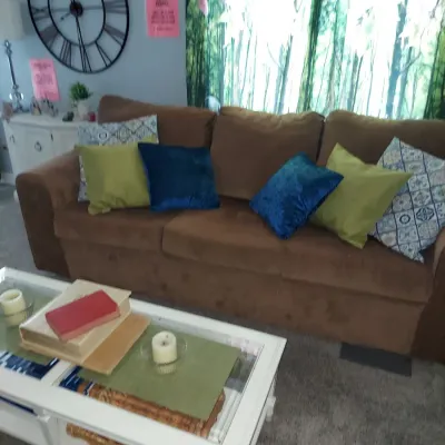 Contemporary brown microfiber sofa styled with blue, green, and patterned throw pillows, paired with a white glass-top coffee table.