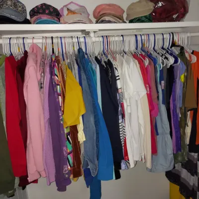 Assorted women's clothing hanging on a closet rod, including jackets, shirts, and sweaters, with a selection of hats arranged on the...