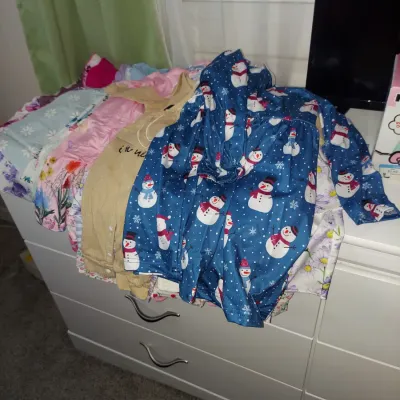 Assorted children's clothing, including a blue snowman-patterned dress, laid out on a white dresser.
