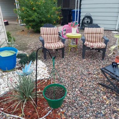Outdoor patio set featuring two dark grey Adirondack-style chairs with striped cushions, a small yellow accent table, and a pink plastic...