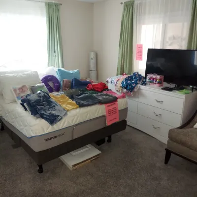 Tempur-Pedic adjustable bed with mattress, shown with various clothing items displayed on top, alongside a white six-drawer dresser...
