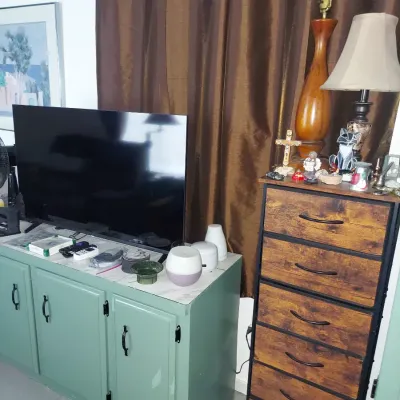 Flat-screen television on a sage green painted media console, paired with a rustic industrial-style seven-drawer chest featuring...