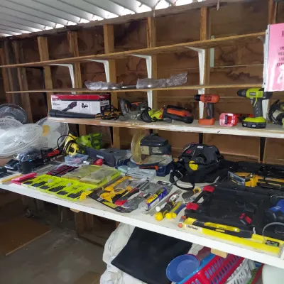 Assorted power tools and hand tools, including drills, circular saws, and drill bit sets, displayed on workshop shelving.