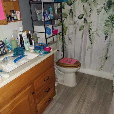 Bathroom vanity with wooden cabinets, a black metal over-the-toilet storage rack, and various personal care items.