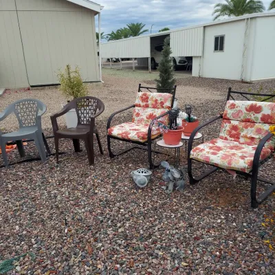 Outdoor patio seating set featuring two black metal armchairs with floral cushions, accompanied by two plastic armchairs in grey and brown.