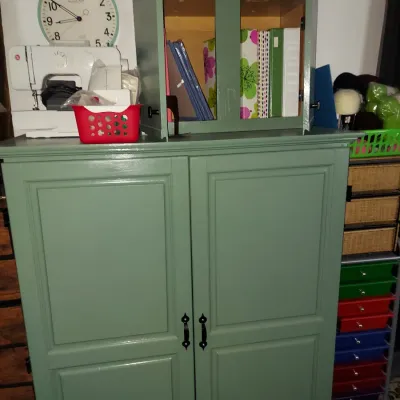 Sage green painted wooden armoire with a matching smaller hutch cabinet on top, shown holding binders and craft supplies.