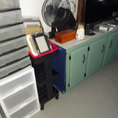 Assorted household items including a black electric table fan, a wooden box, plastic storage drawers, and a black rolling utility cart.