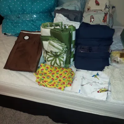 Assortment of folded bedding and linens, including a teal polka dot comforter, dog-patterned sheets, and various colorful duvet covers...