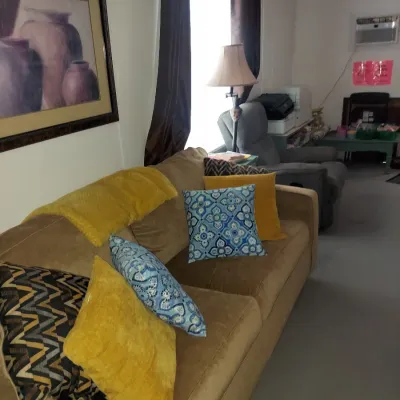 Contemporary tan microfiber sofa adorned with an assortment of blue, yellow, and patterned throw pillows, shown alongside a framed art...