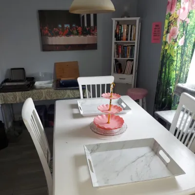 White wooden dining table set with matching chairs, featuring a pink three-tiered serving stand and marble-patterned trays.