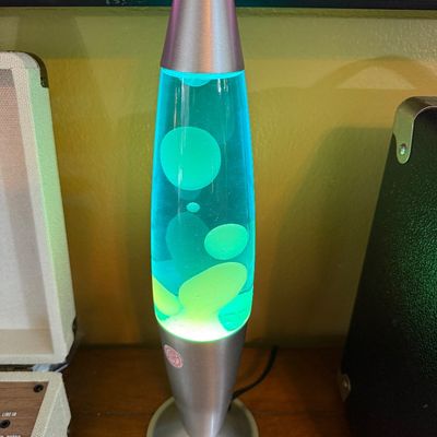 Vintage-style rocket lava lamp with a brushed silver metal base and cap, featuring green wax in blue liquid.