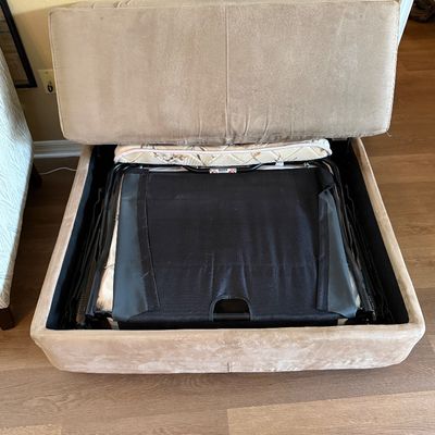 Beige microfiber sleeper ottoman shown open to reveal the folded twin-size mattress and pull-out mechanism inside.