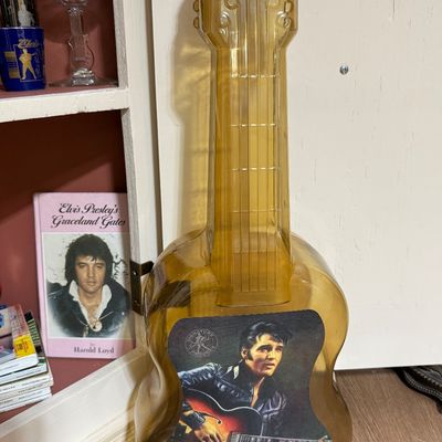 Vintage Elvis Presley guitar-shaped amber  decanter with a portrait label of Elvis playing guitar, shown alongside other Elvis memorabilia.