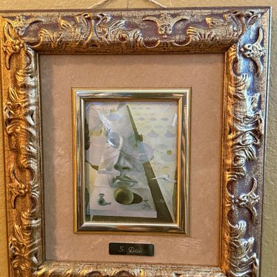 Small framed Salvador Dalí print featuring a surrealist face, housed in an ornate, crackle-finish gold frame with a nameplate.