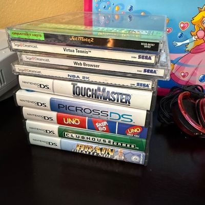 Stack of vintage video games including PlayStation Greatest Hits Jet Moto 2, Sega Dreamcast titles, and various Nintendo DS games, shown...