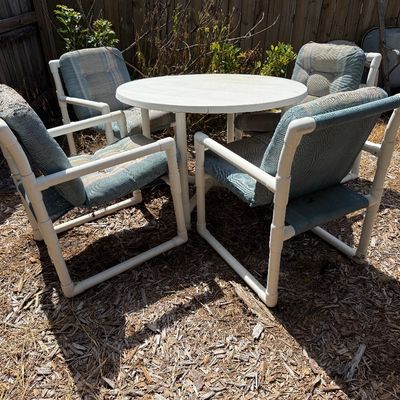 Vintage PVC pipe patio set featuring a round white table and four matching armchairs with blue cushions.